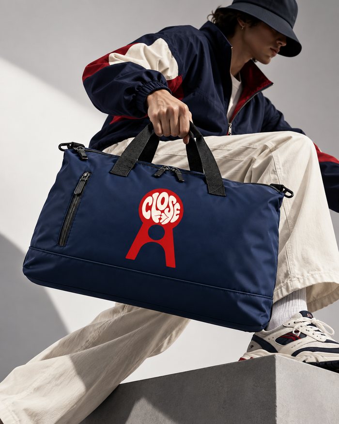 Bolsa azul-marinho com o logo Close nas mãos de uma pessoa de chapéu bucket