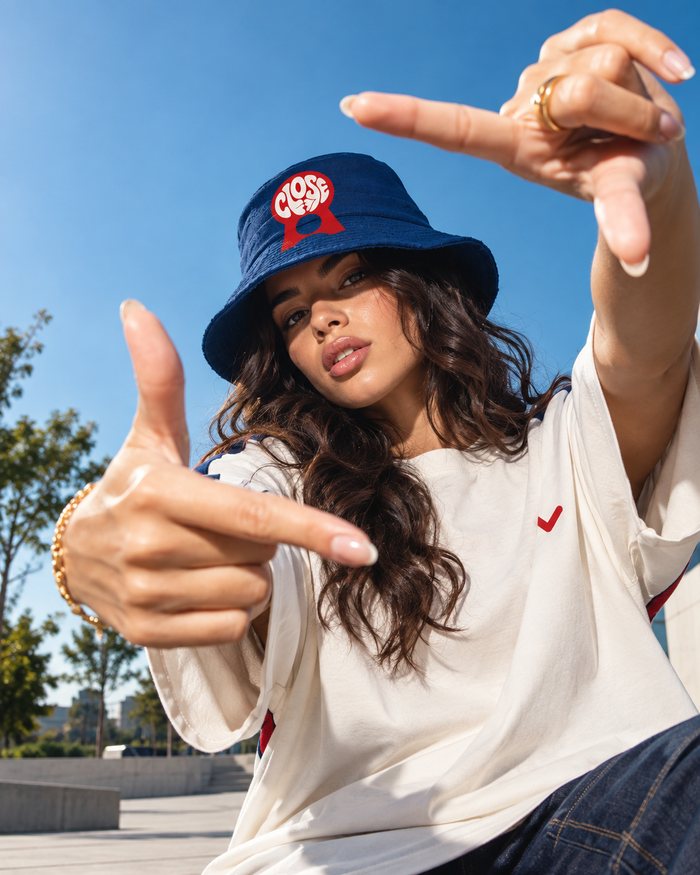 Jovem de chapéu bucket azul com o logo Close fazendo uma moldura com as mãos